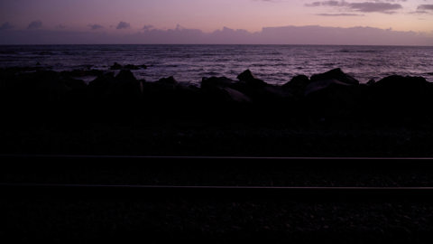 A purple sunset, outlines of rocks are in the foreground but are covered by the shadow 