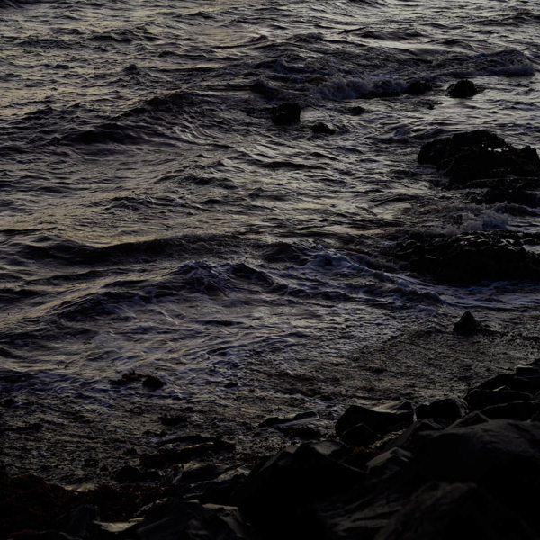A dark ocean with only the waves and rock shadows recognisable.