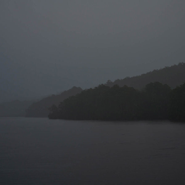 A dark, rainy image of a body of water surrounded by the wilderness